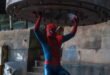 Tom Holland en Spider-Man, costume rouge et bleu, soulevant à bout de bras un lourd disque de métal boulonné