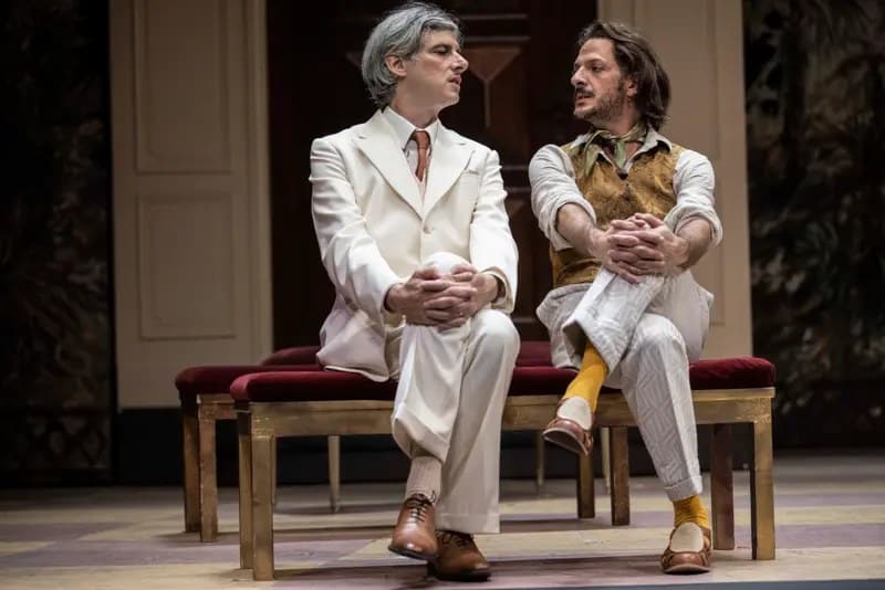 Micha Lescot, en costume blanc, et Vincent Dedienne, en gilet et pantalon clair, assis côte à côte sur une banquette.